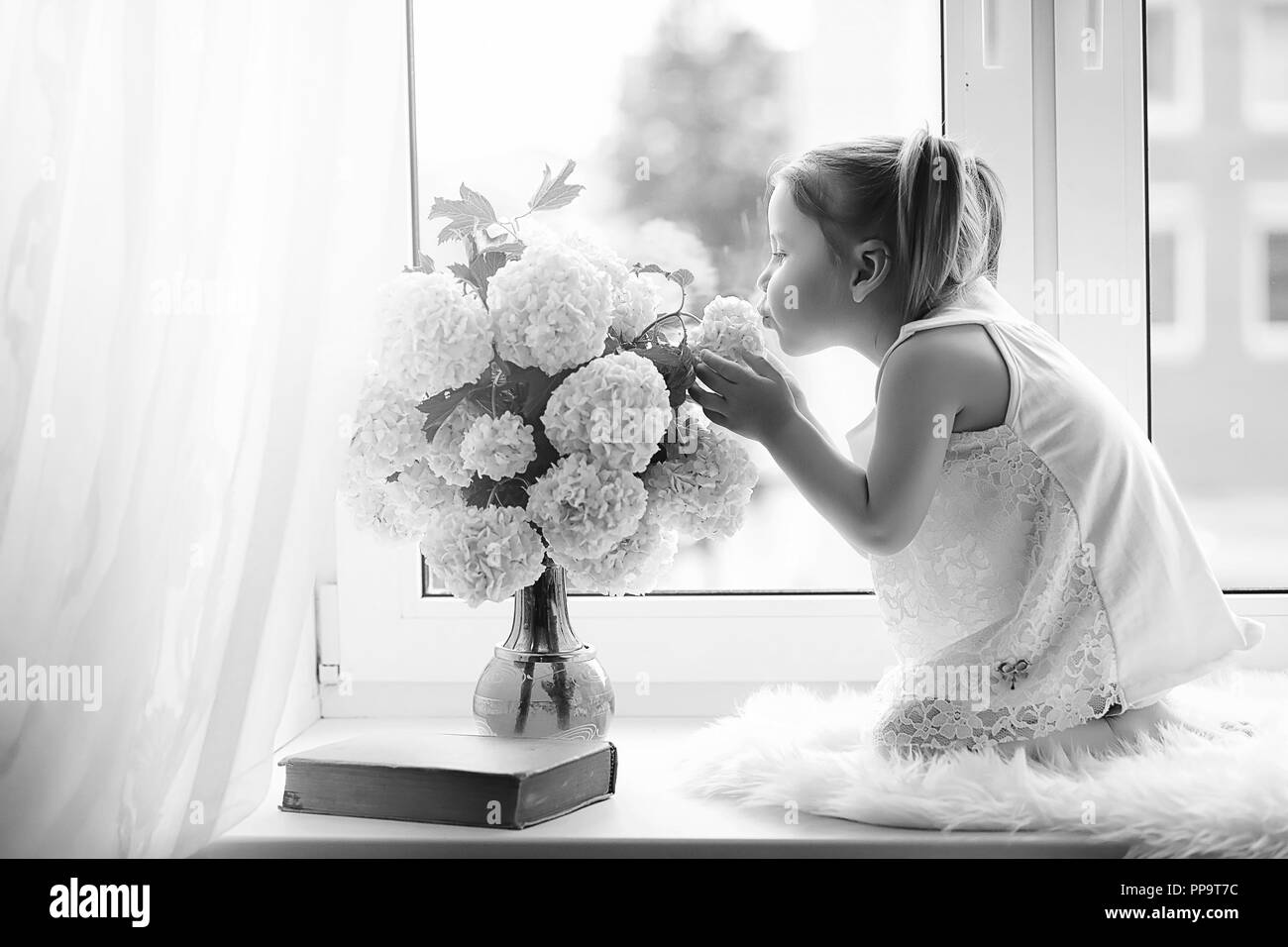 La bambina è seduta sul davanzale. Un mazzo di fiori Foto Stock