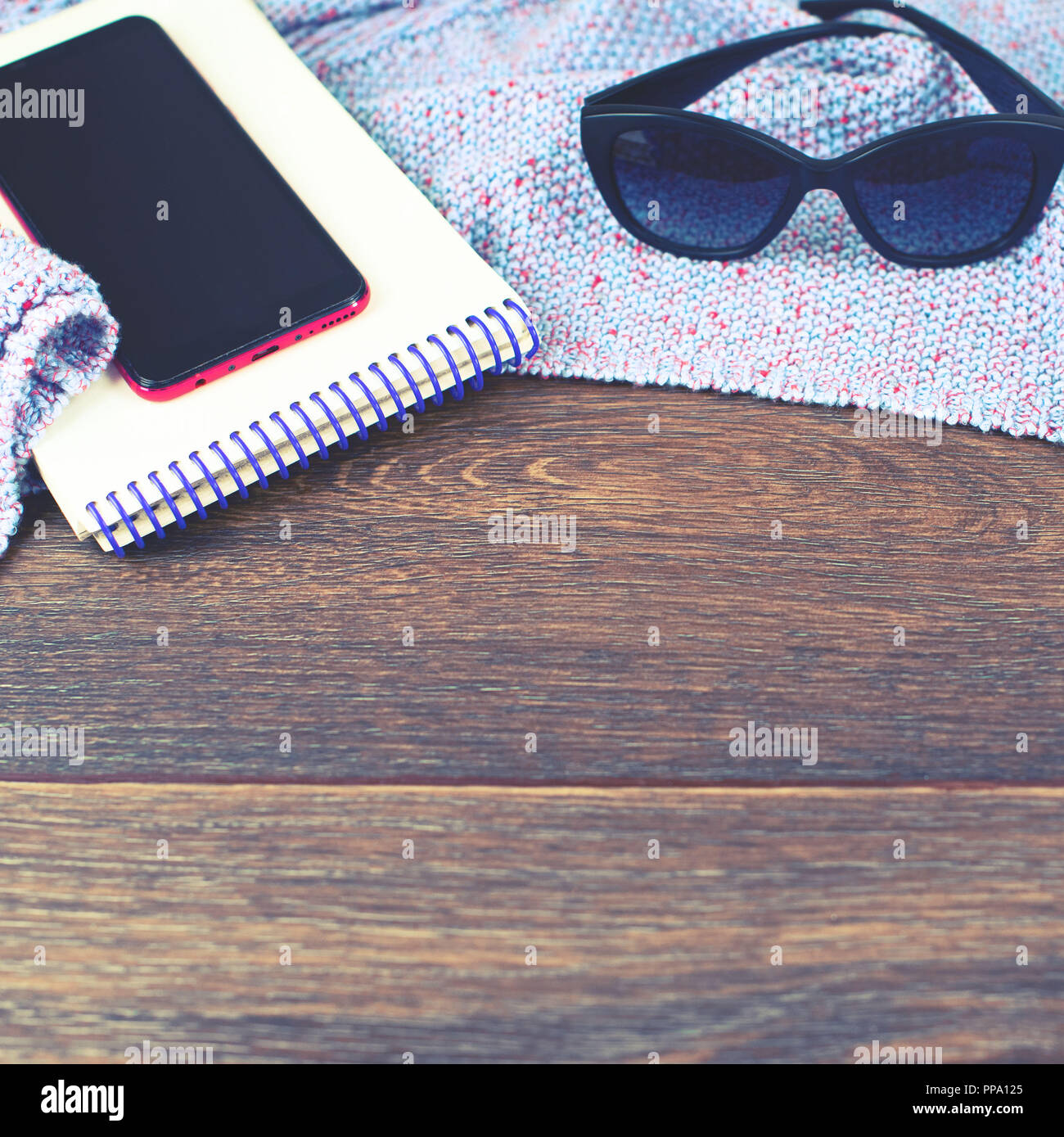 Spazio vuoto sul desktop mobile phone gadget Notepad occhiali da sole. Il vecchio legno naturale sfondo squallido coperta di maglia plaid color porpora tonificante Foto Stock