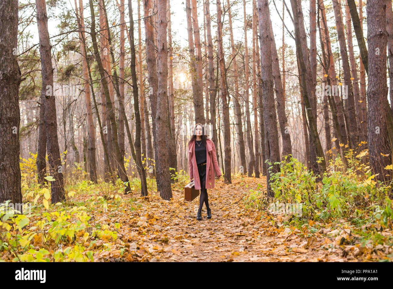 Autunno, moda, persone concetto - donna marrone con valigia retrò a piedi attraverso il parco di autunno e sorridente Foto Stock