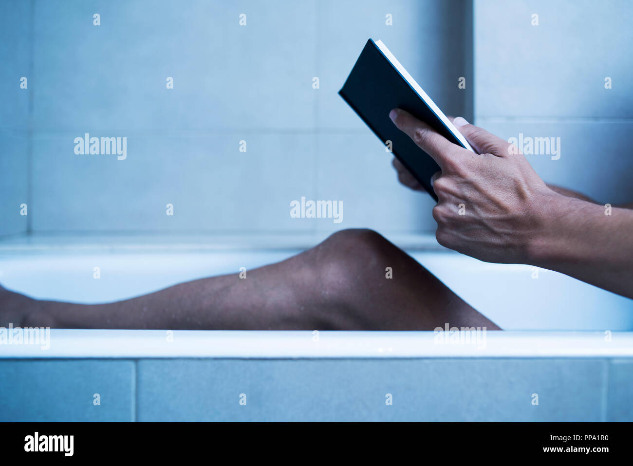 Primo piano di un giovane uomo caucasico leggendo un libro in una vasca da bagno in una misteriosa atmosfera, con un effetto drammatico Foto Stock