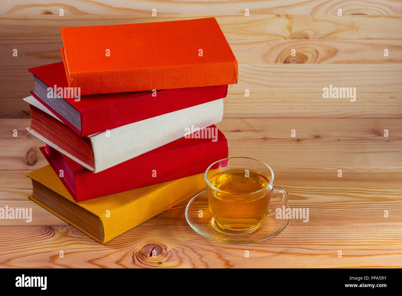 Bicchiere di vetro con tè e una pila di libri con copertine colorate Foto Stock