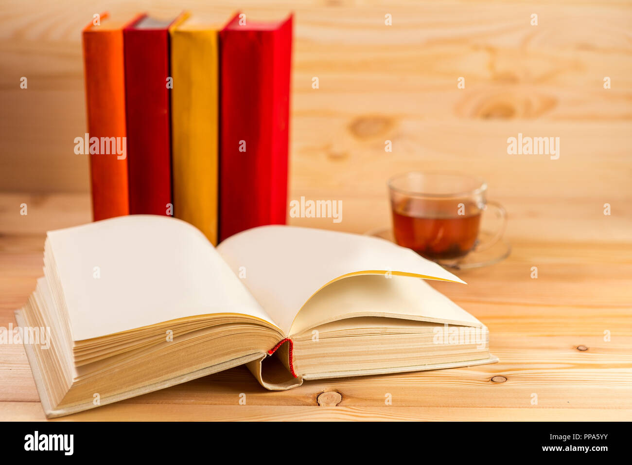 Libro Aperto e vetro tazza di tè e una pila di libri con custodie colorate. Foto Stock