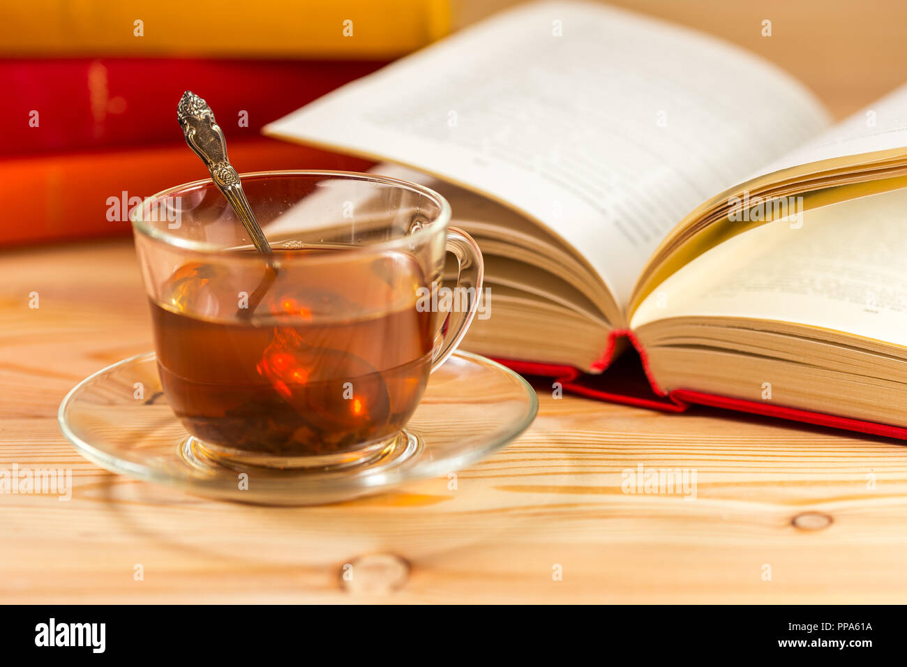Libro Aperto e vetro tazza di tè e una pila di libri con custodie colorate. Foto Stock