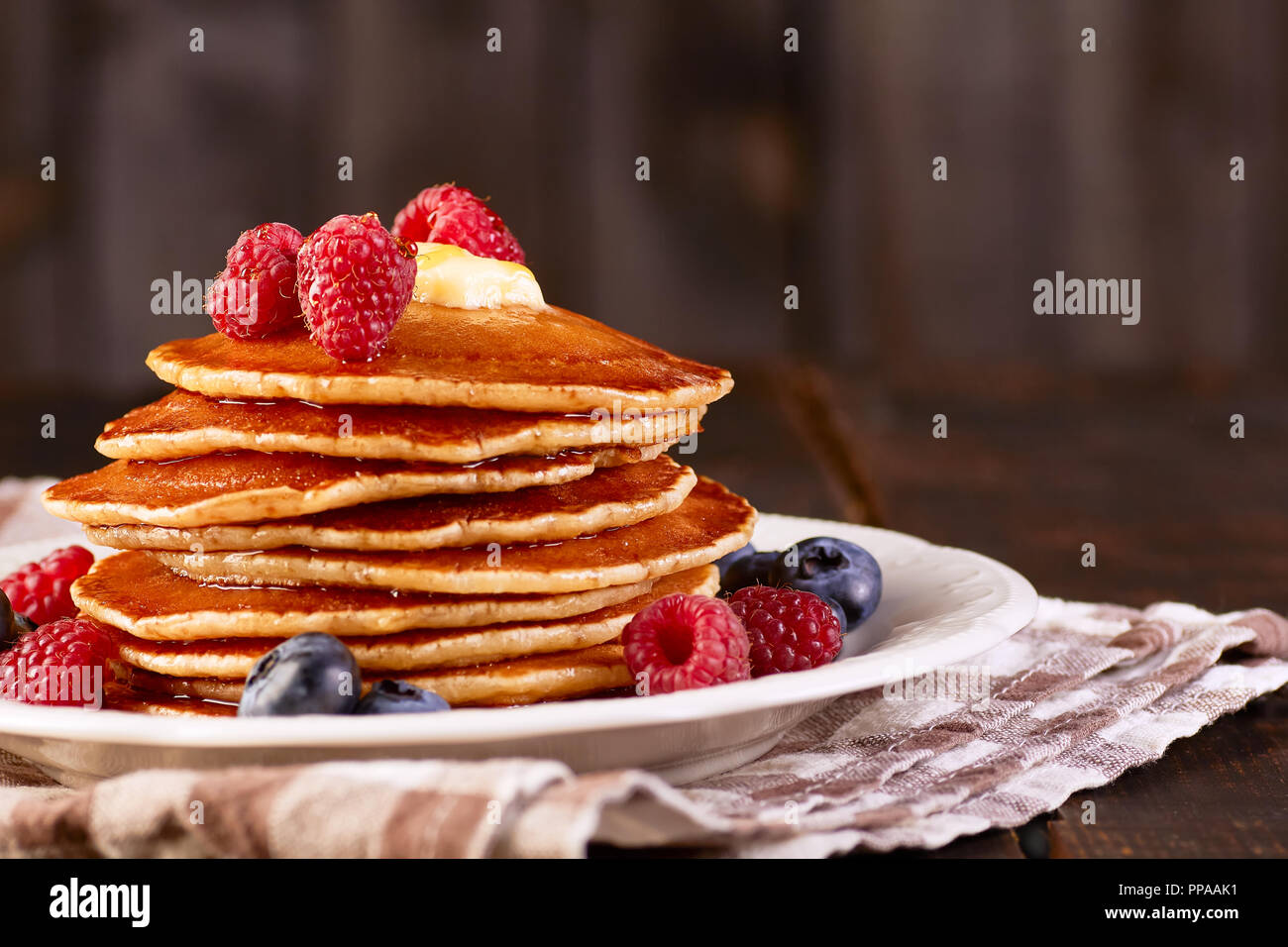 Frittelle con le bacche e sciroppo d'acero sul piatto su tovagliolo tessili Foto Stock