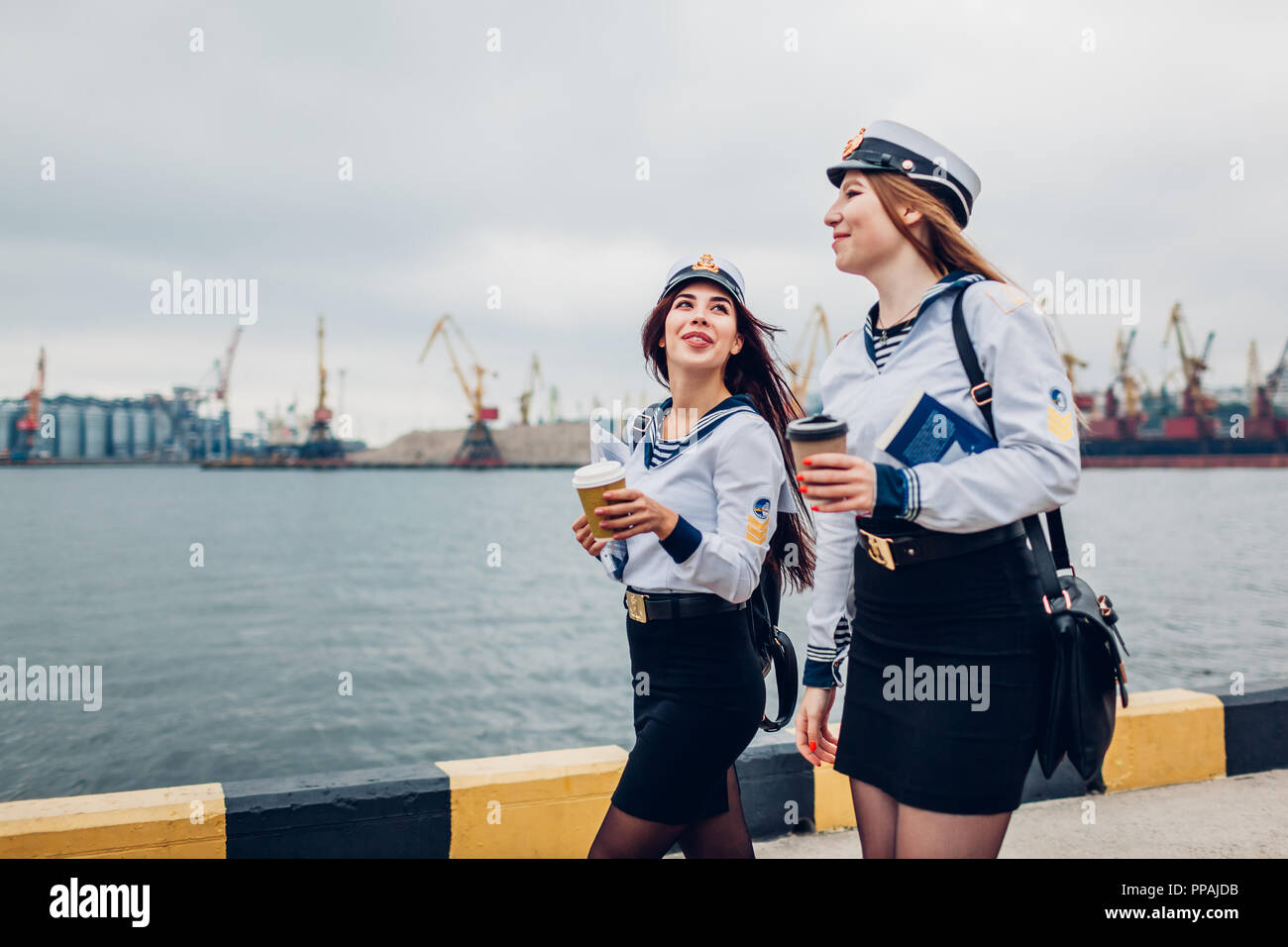 Due college studenti donne di Marine Academy a piedi dal mare indossando uniforme. Amici camminare, parlare e bere caffè Foto Stock