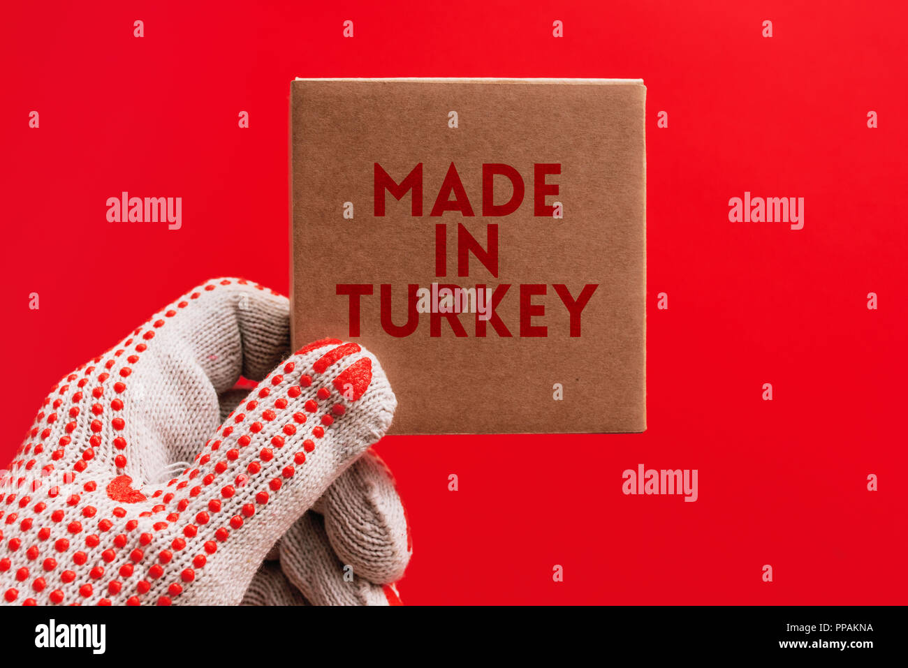 Fabbricato in Turchia, lavoratore con dei guanti di protezione in cartone di contenimento prodotto pacchetto su sfondo rosso che è il colore primario del cittadino turco fla Foto Stock