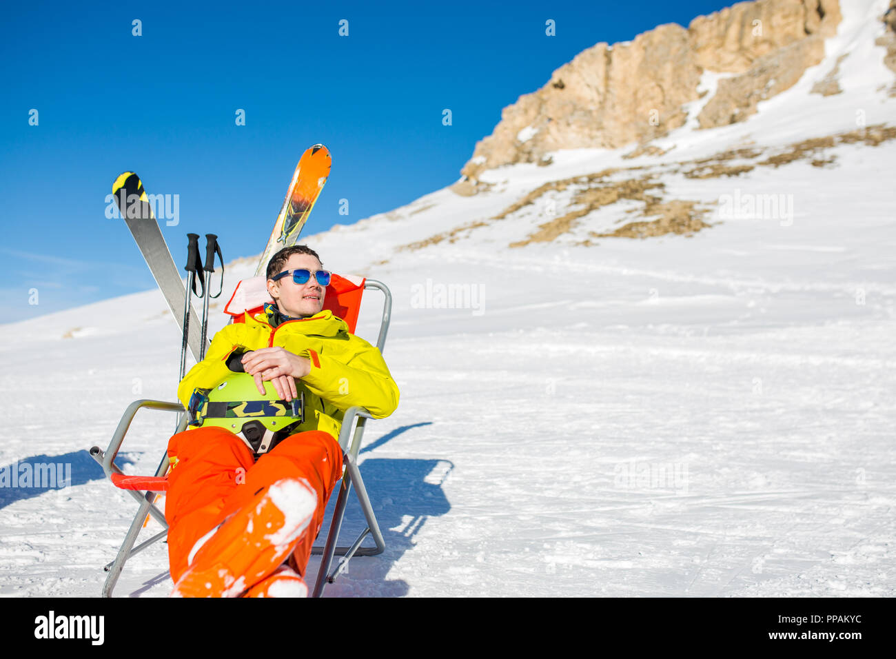Immagine di sport uomo seduto sulla sedia accanto a sci e bastoni sullo sfondo di montagne innevate Foto Stock