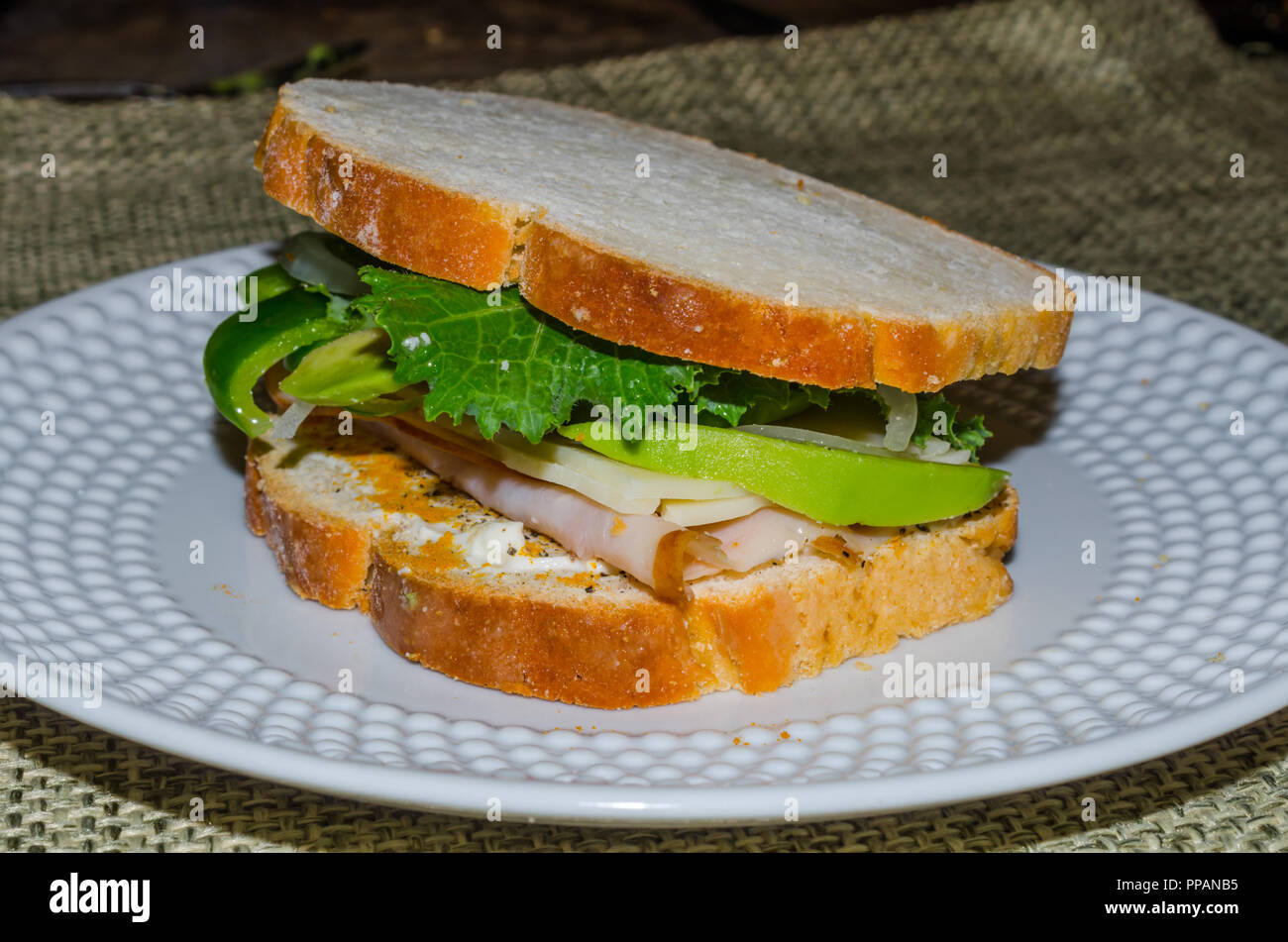 Home pane cotto affettato per creare sandwich riempito con la Turchia, avocado, cresciuto in casa pepe verde e Kale. Nutriente delizioso pranzo o cena. Foto Stock