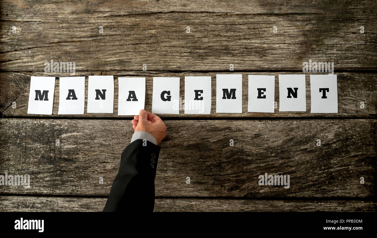 Vista superiore del manager mano disponendo dieci carte bianche con lettere su di essi in una linea per formare una parola sul management antichi testurizzata di tavole di legno. Foto Stock