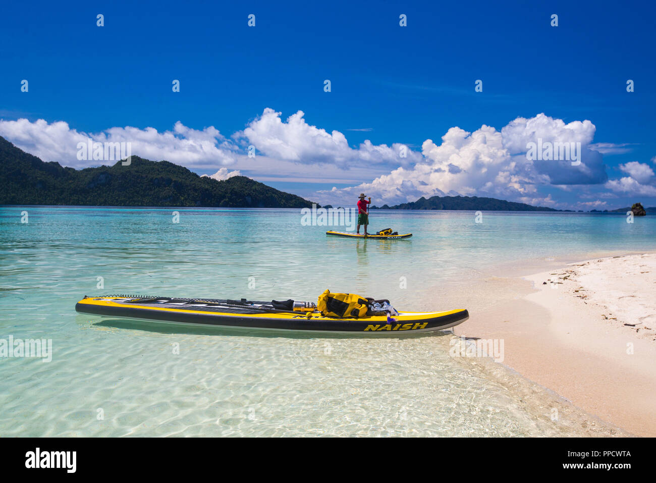 Vista in lontananza paddleboarding uomo in mare vicino spiaggia, Misool Raja Ampat, Indonesia Foto Stock