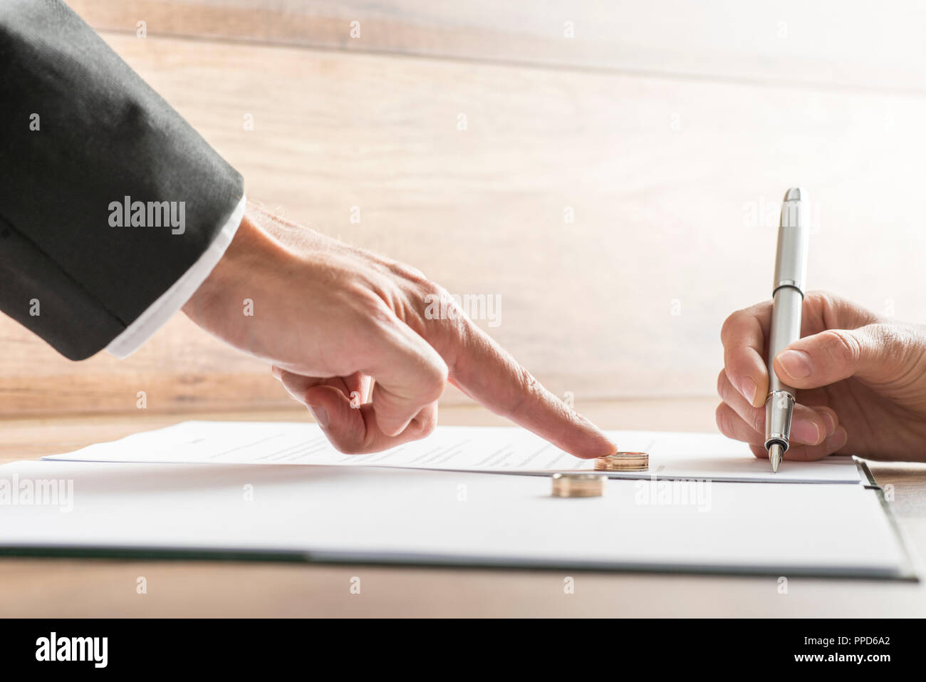 Maschio di spinta a mano un anello di nozze oltre ad una mano femminile circa a firmare documenti di divorzio. Concettuale del divorzio o di matrimonio. Foto Stock