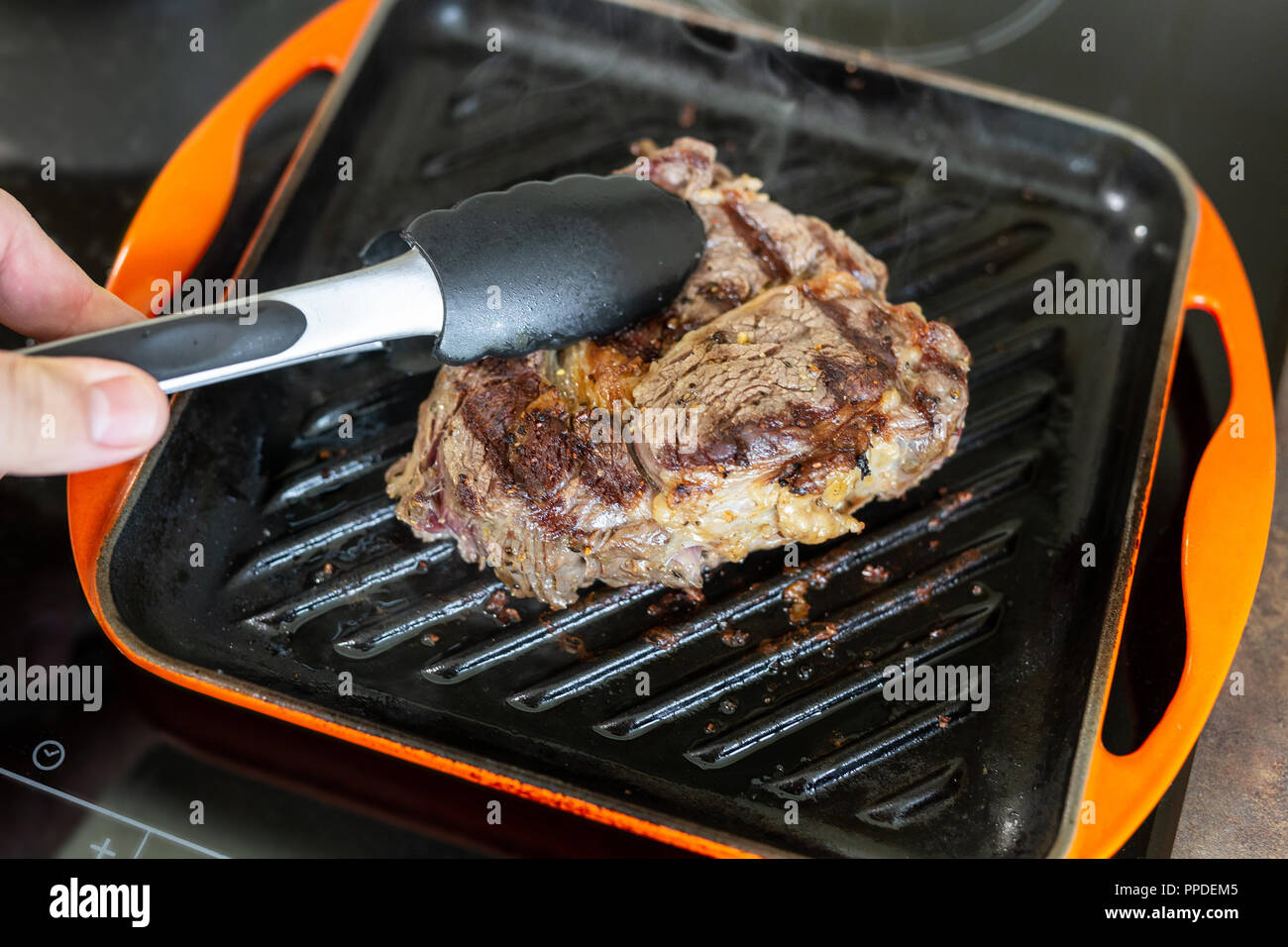 La cottura della carne in ghisa padella per grigliare all'interno di home.  Persona girando ribeye su altro lato con le pinze Foto stock - Alamy