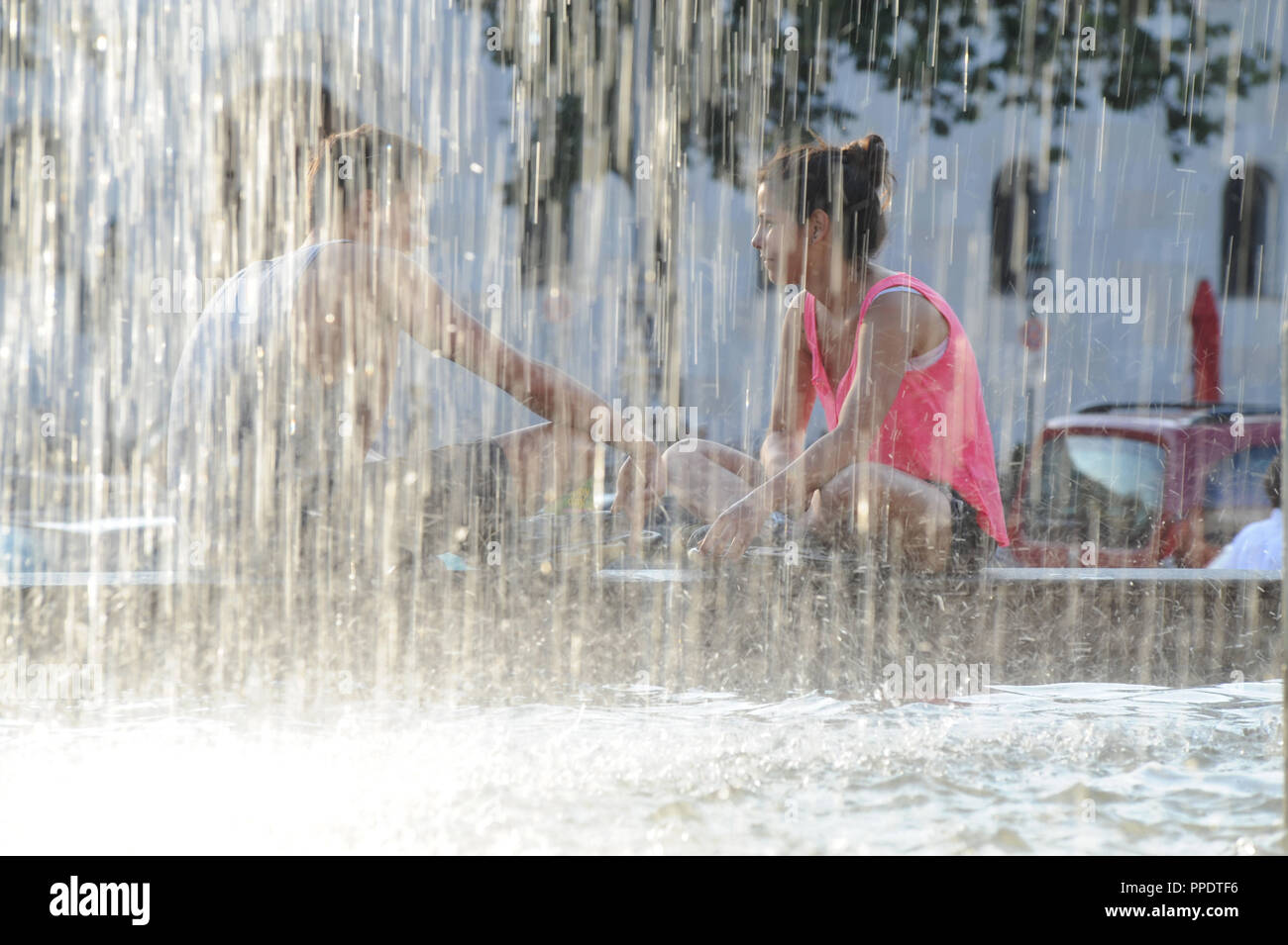Gli studenti godono l'estate e dei getti d'acqua della fontana a Geschwister-Scholl-Platz Foto Stock