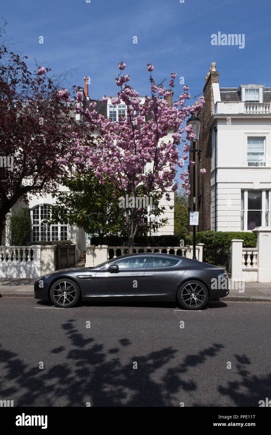 Aston Martin parcheggiata di fronte costoso case con alberi in fiore. Foto Stock