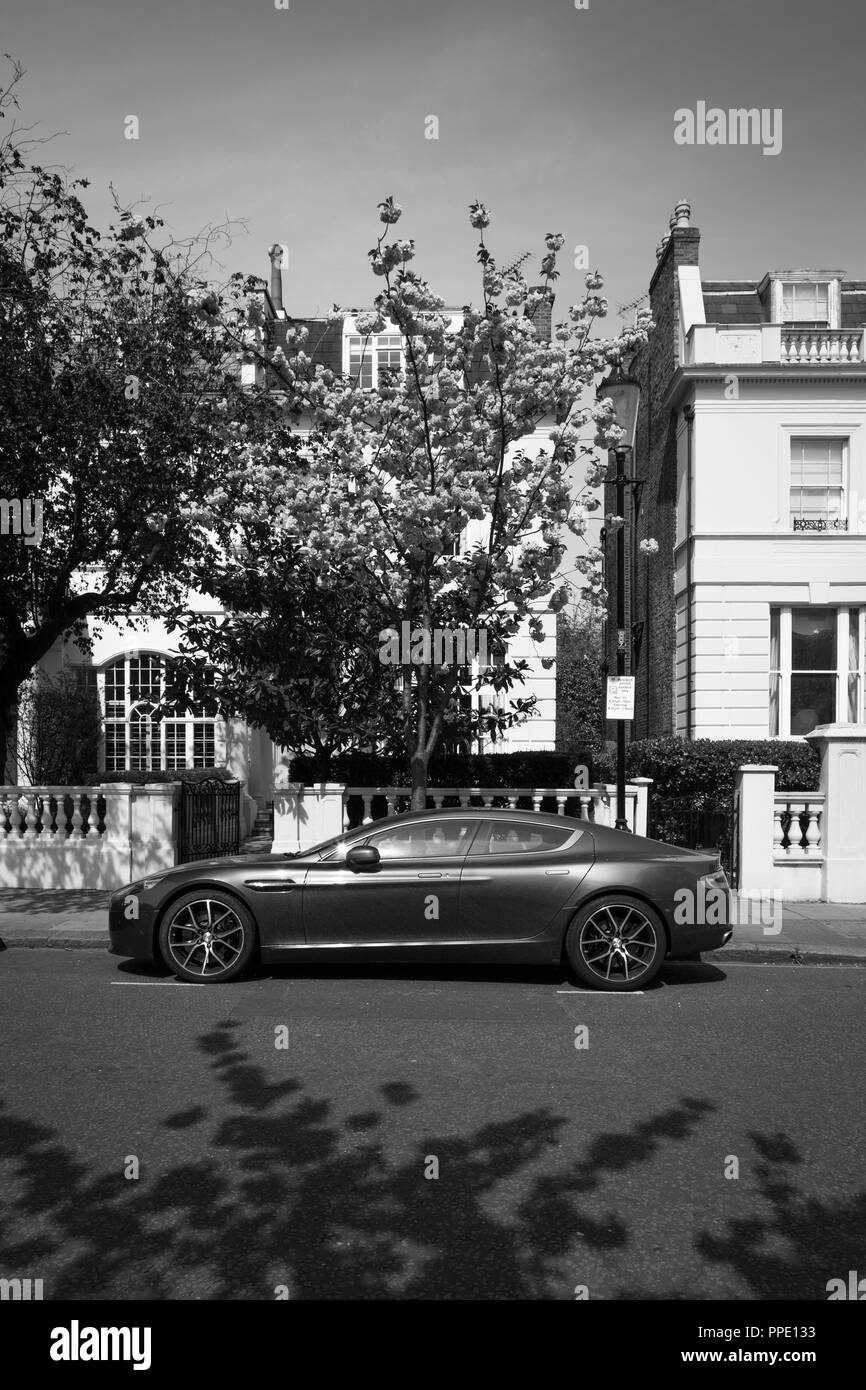 Aston Martin parcheggiata di fronte costoso case con alberi in fiore. Foto Stock