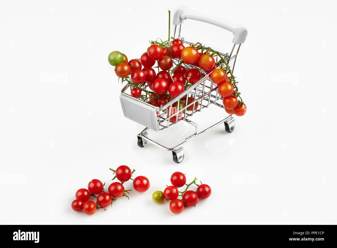 Mini carrello pieno con pomodori ciliegia su sfondo bianco. Spazio di copia Foto Stock