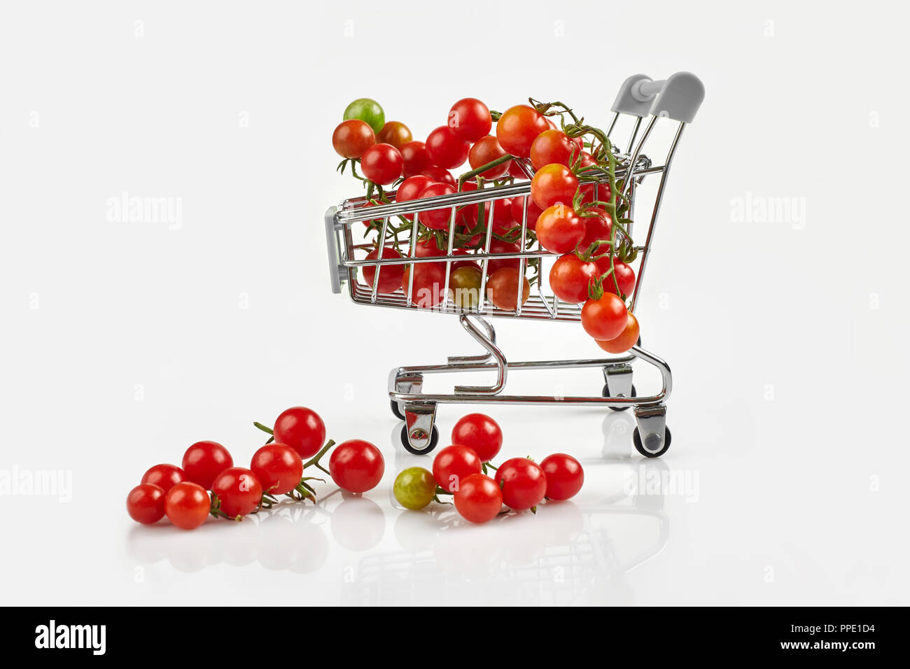Mini carrello pieno con pomodori ciliegia su sfondo bianco. Spazio di copia Foto Stock