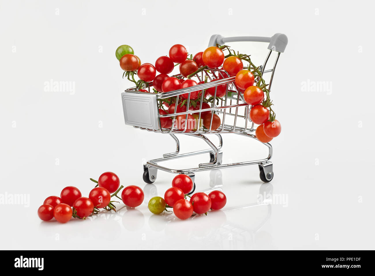 Mini carrello pieno con pomodori ciliegia su sfondo bianco. Spazio di copia Foto Stock