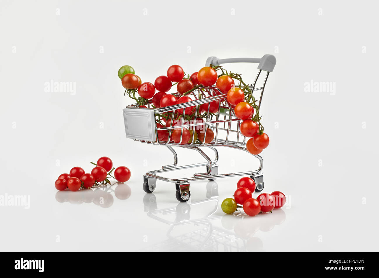 Mini carrello pieno con pomodori ciliegia su sfondo bianco. Spazio di copia Foto Stock