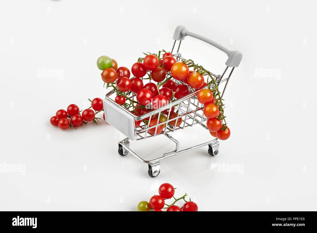 Mini carrello pieno con pomodori ciliegia su sfondo bianco. Spazio di copia Foto Stock