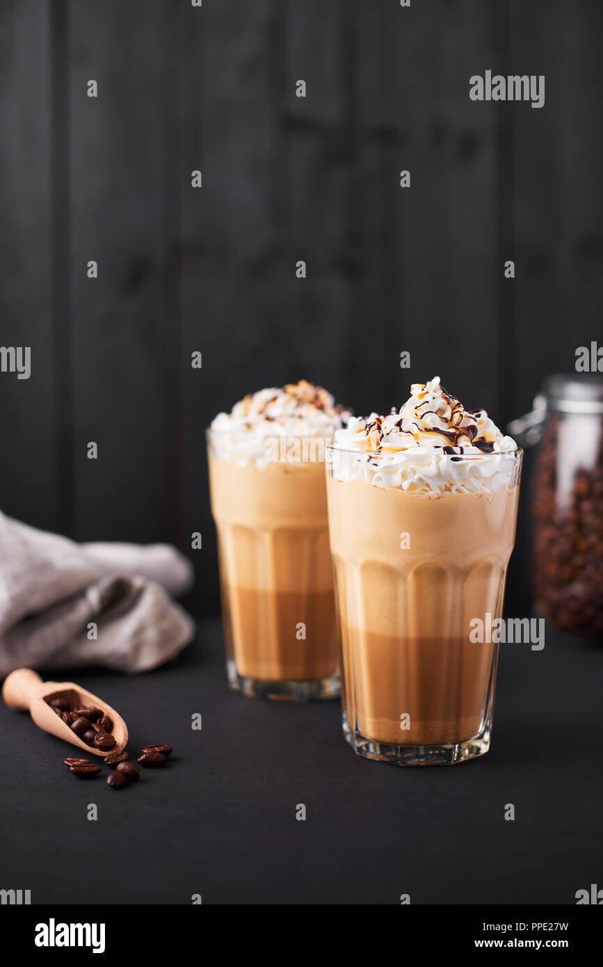 Iced caramello latte caffè in un bicchiere alto con lo sciroppo al cioccolato e panna montata. Legno scuro dello sfondo con copia spazio. Foto Stock