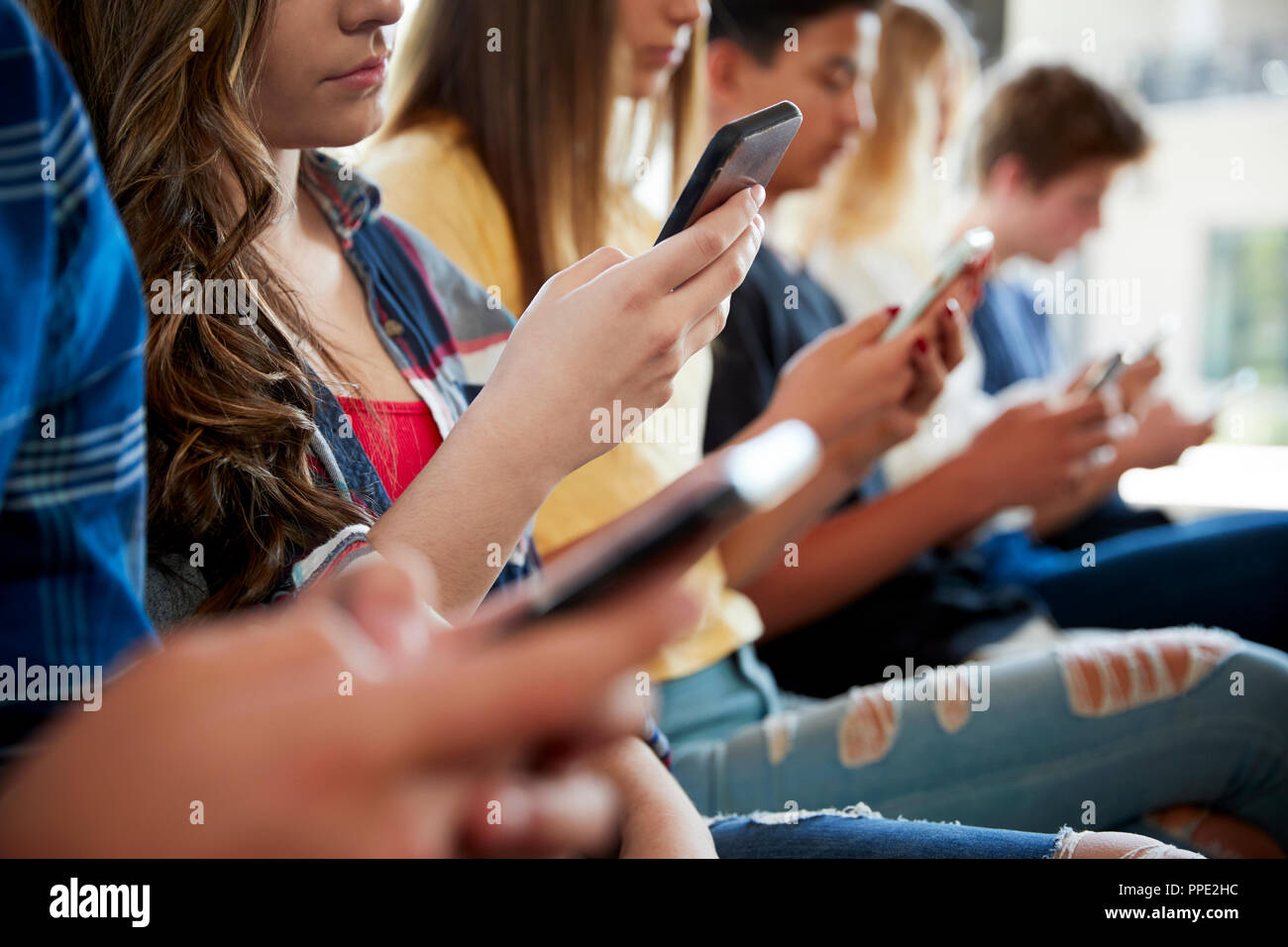 In prossimità di una linea di alta scuola gli studenti utilizzando i telefoni cellulari Foto Stock