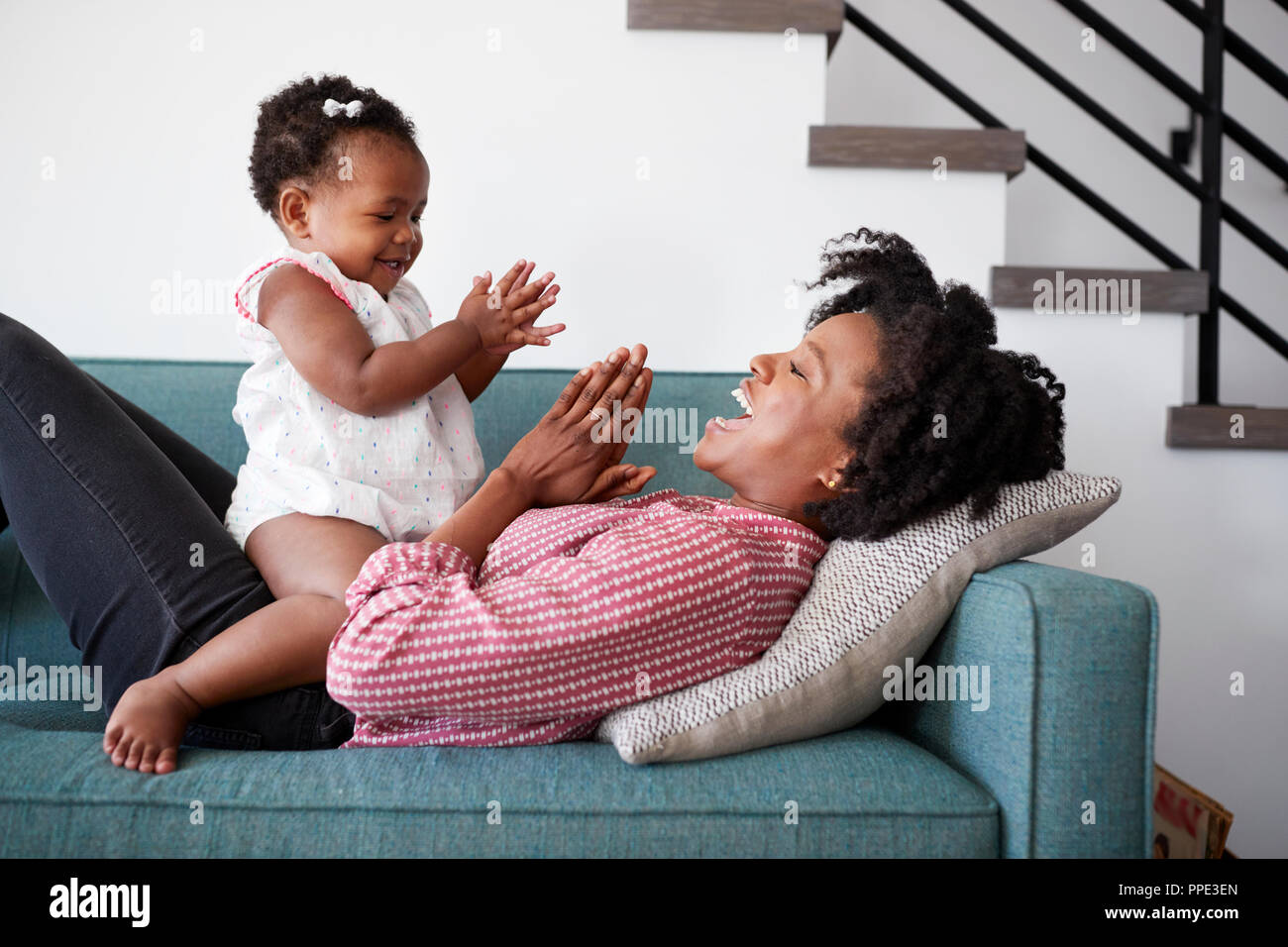 Madre sdraiato sul divano di casa a giocare battendo le mani di gioco con la nostra bambina Foto Stock