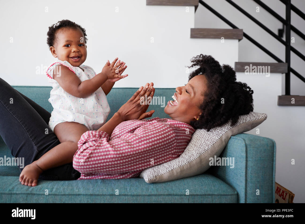 Madre sdraiato sul divano di casa a giocare battendo le mani di gioco con la nostra bambina Foto Stock