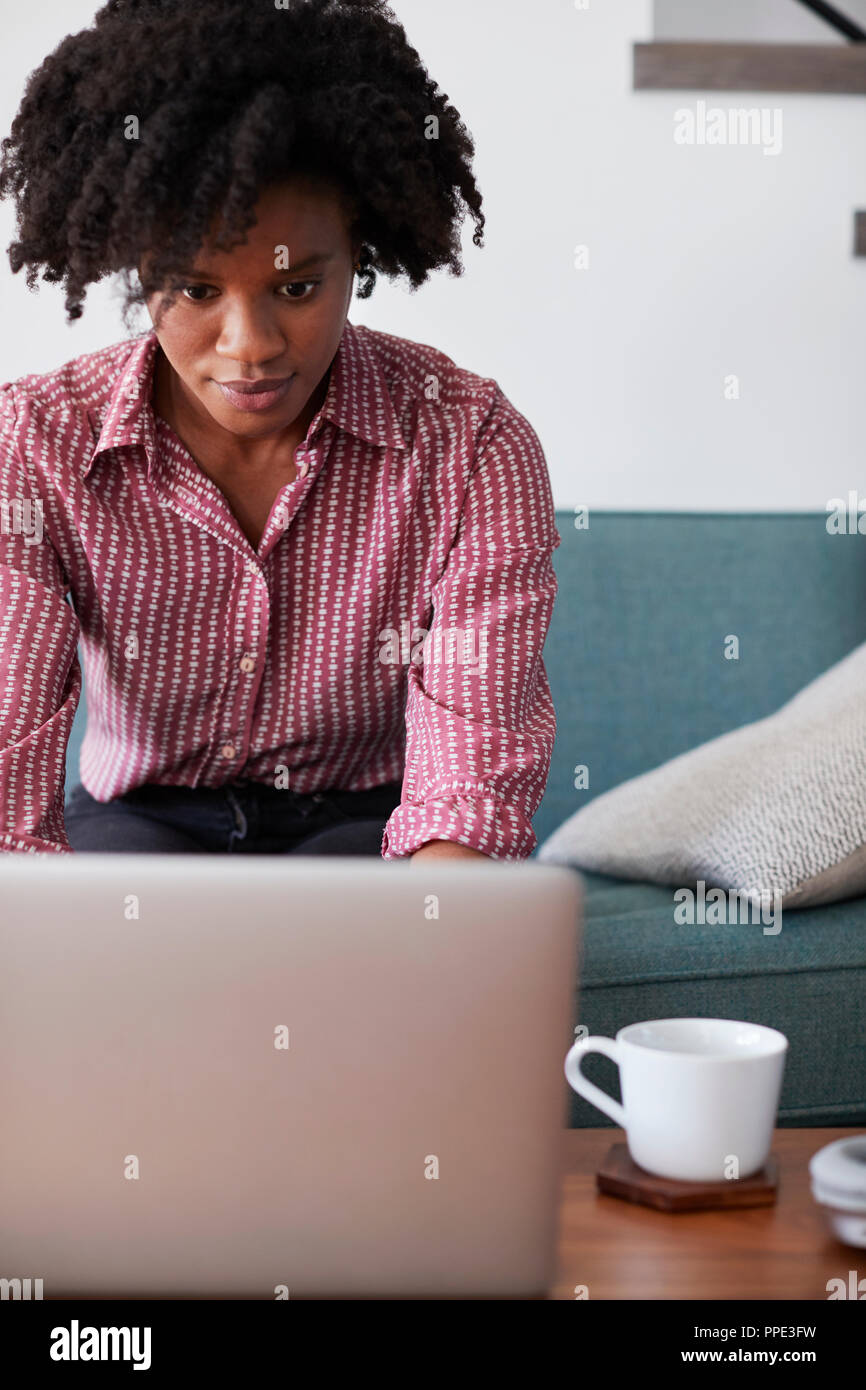 Donna seduta su un divano di casa utilizzando il computer portatile Foto Stock