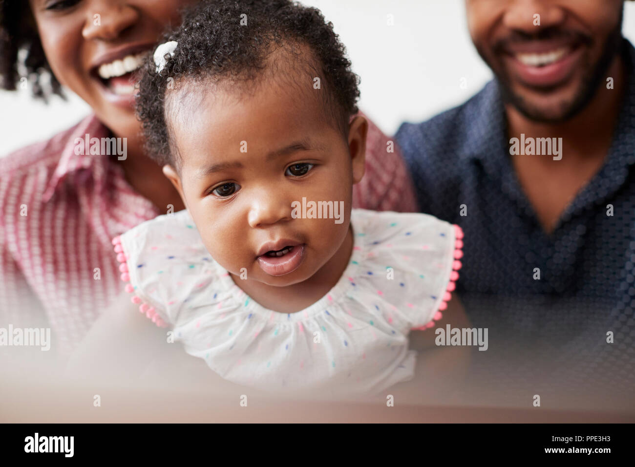 Famiglia con la nostra bambina seduti sul divano di casa Guardando il computer portatile Foto Stock