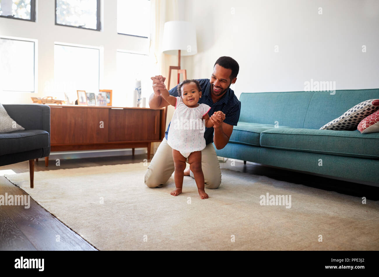 Padre incoraggiando la nostra bambina di prendere i primi passi a casa Foto Stock