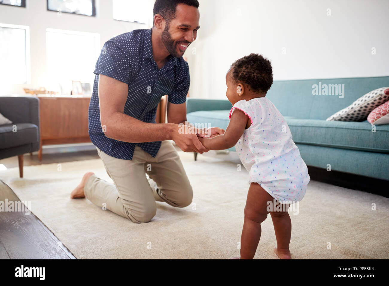 Padre incoraggiando la nostra bambina di prendere i primi passi a casa Foto Stock