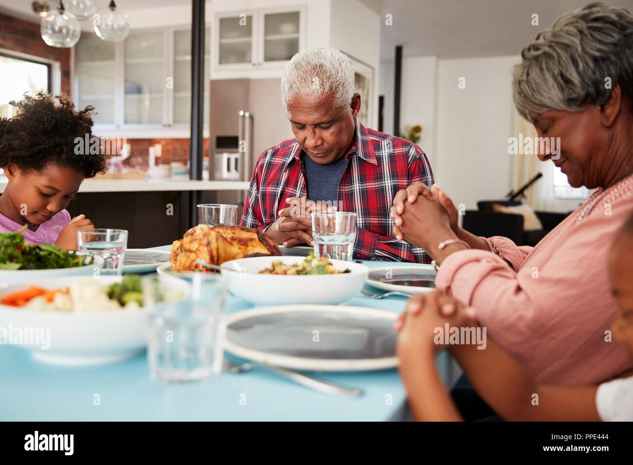Nonni pregare prima di pasto a casa con nipoti Foto Stock