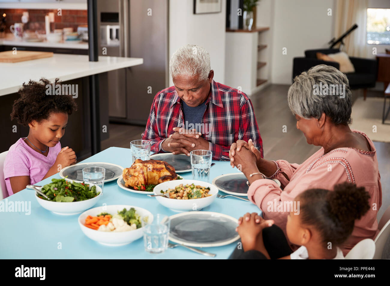 Nonni pregare prima di pasto a casa con nipoti Foto Stock