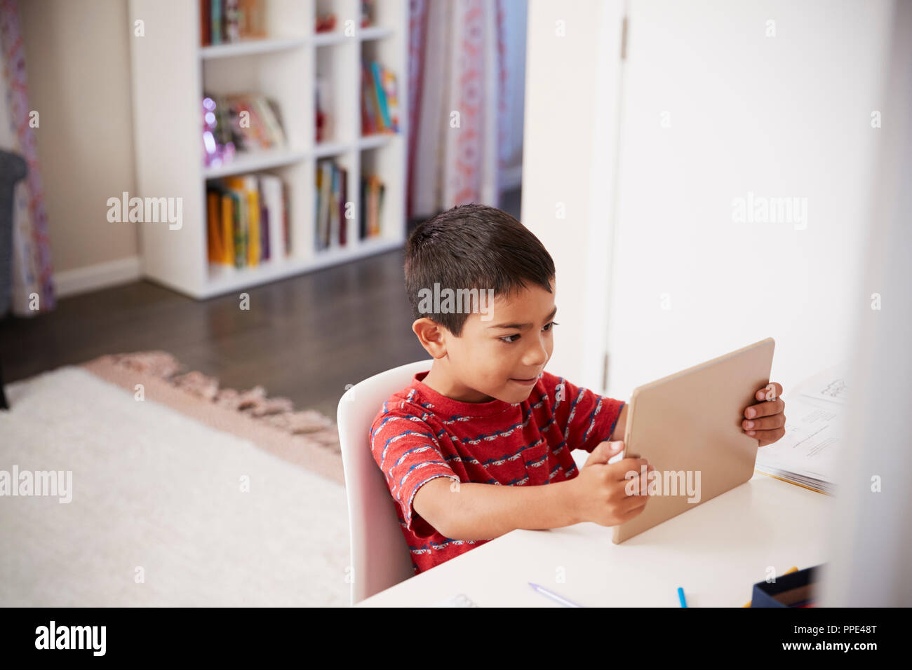 Ragazzo seduto alla scrivania in camera da letto utilizzando tavoletta digitale per fare i compiti Foto Stock