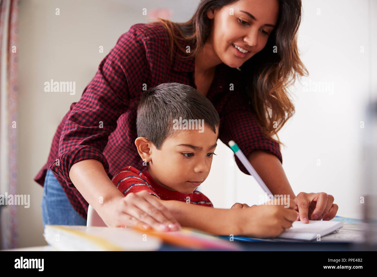 Madre aiutare figlio con compiti seduto alla scrivania in camera da letto Foto Stock