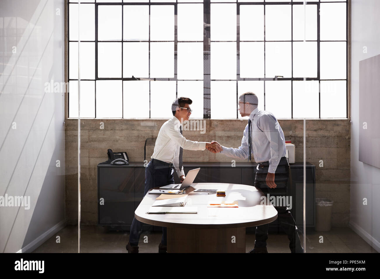 Due imprenditori stand stringono le mani in un ufficio, vista laterale Foto Stock