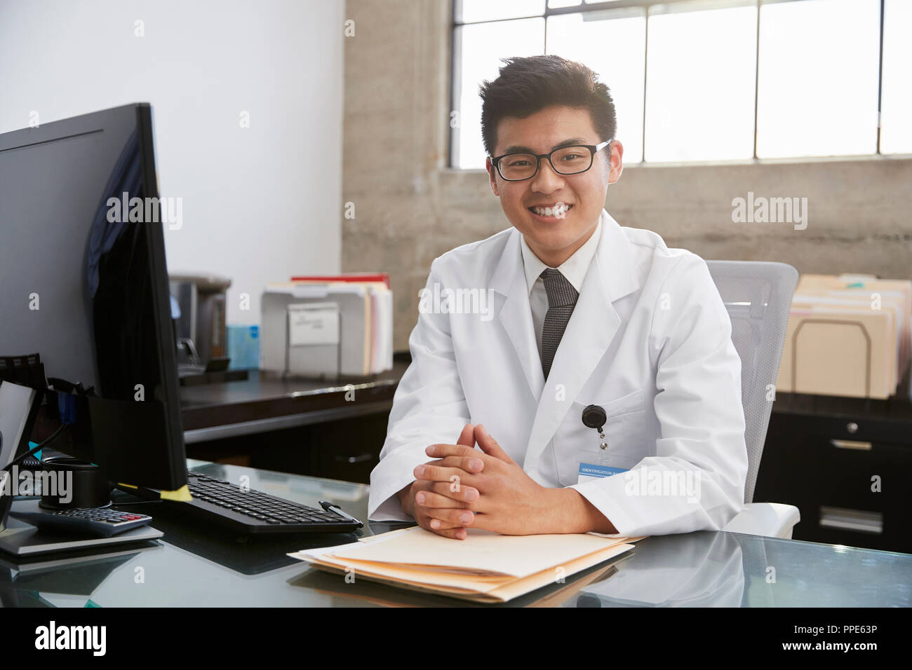 Giovani asiatici medico maschile seduto alla scrivania, ritratto Foto Stock