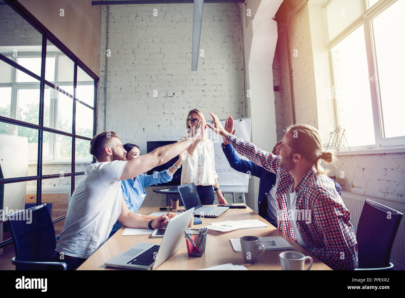 Felice successo multirazziale team aziendali fornendo un alto cinque gesto come ridono e allietare il loro successo. Foto Stock