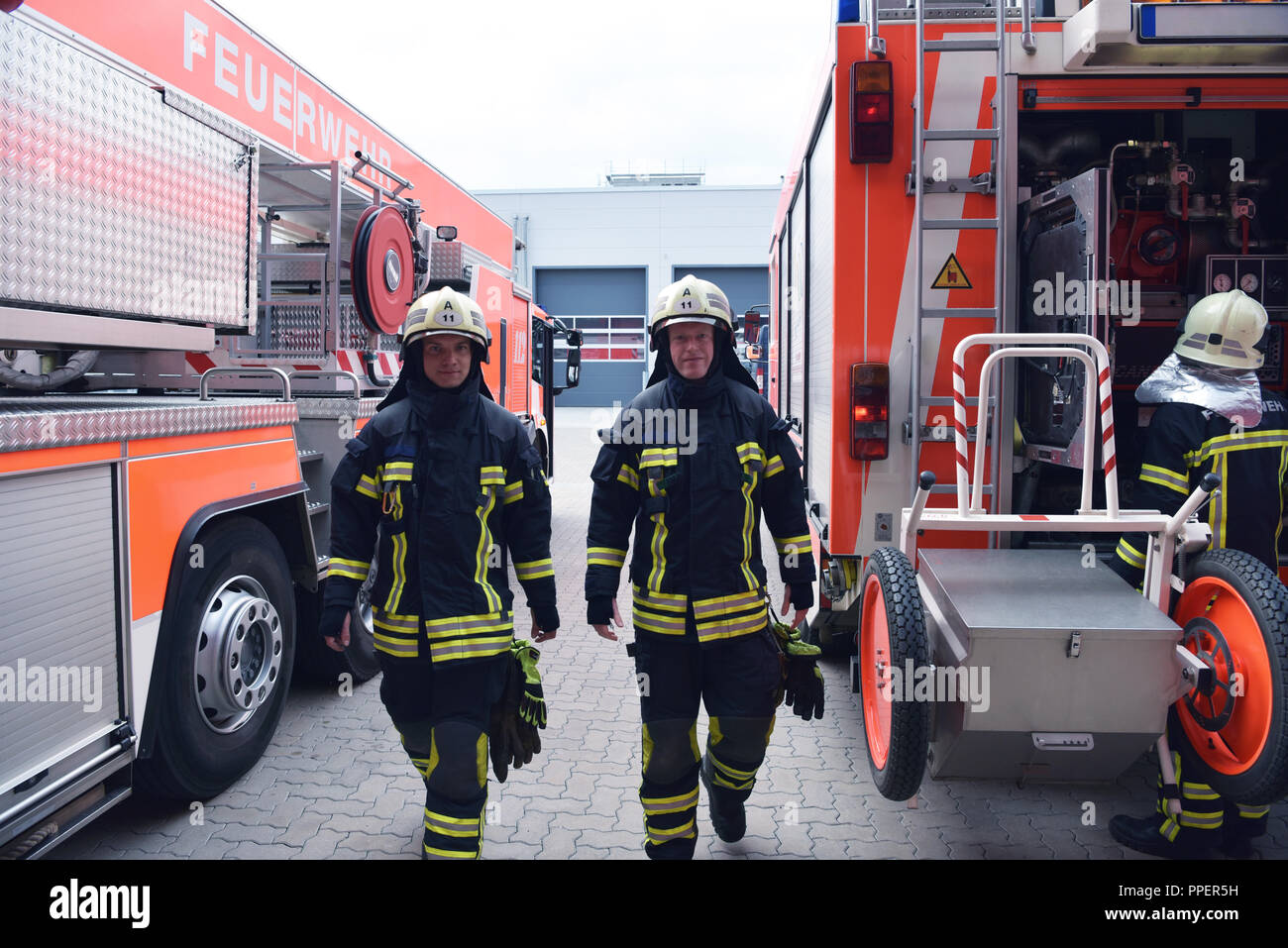Gruppo di vigili del fuoco in corrispondenza del veicolo di emergenza nella stazione dei vigili del fuoco Foto Stock