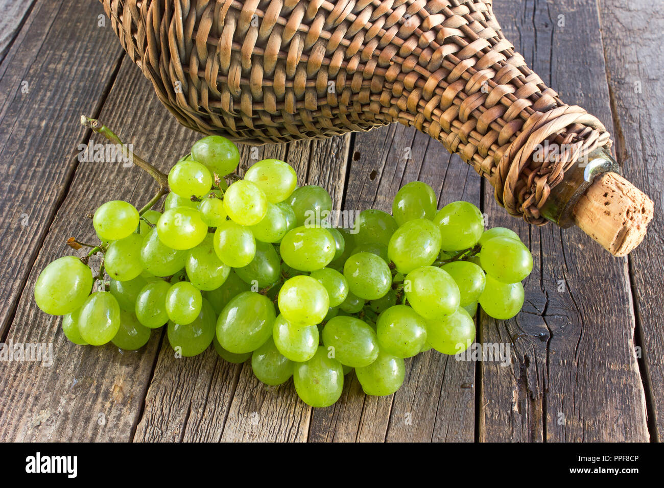 Uva bianca con il vecchio avvolto in vimini bottiglia di vetro sul tavolo di legno Foto Stock