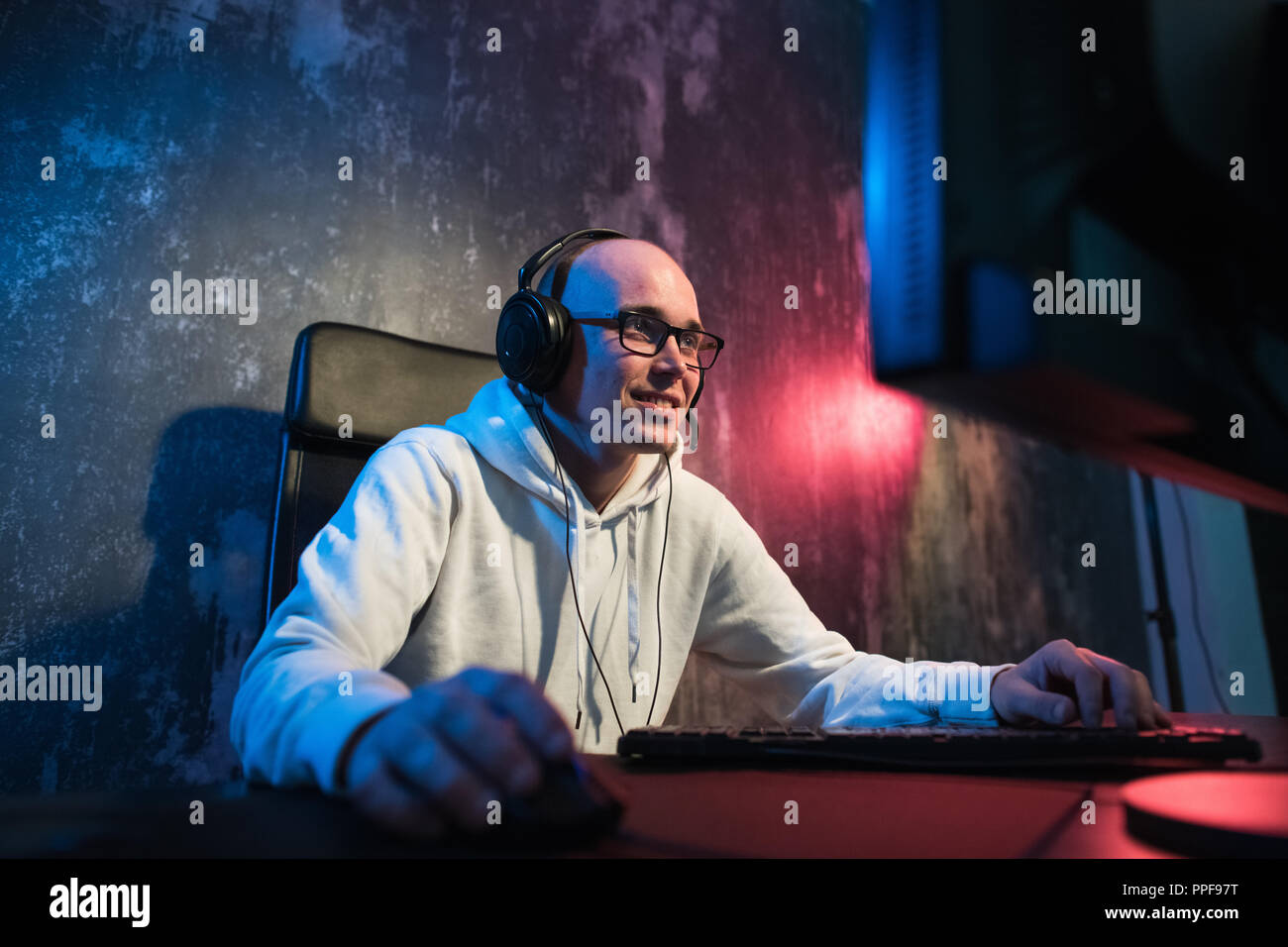 Ritratto di un giovane gioiosa gamer per giocare con i videogiochi in casa su un computer. Gamer in cuffie è felice e che mostra i pollici fino gesto perché ha vinto il gioco. Giochi di Computer concetto. Foto Stock