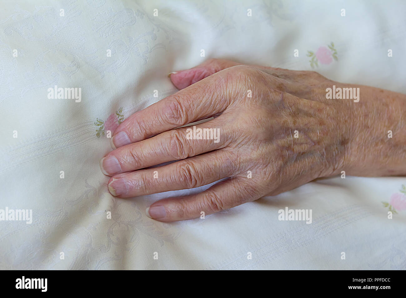 Uno scarno mano di una vecchia donna con una malattia terminale come il cancro su un leggero piumone, concetto di morte, morente Foto Stock