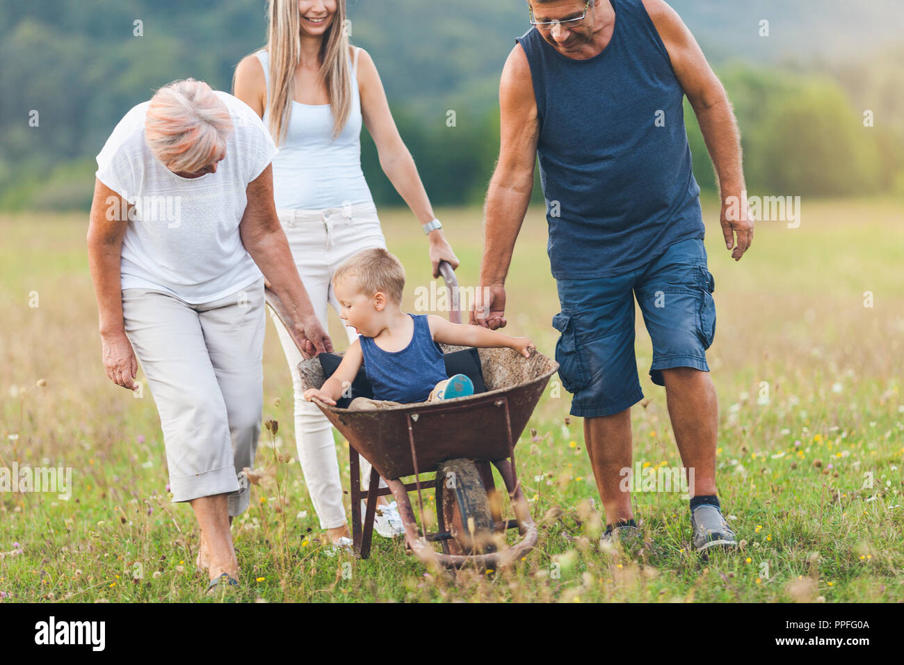 Famiglia spingendo il loro bambino piccolo e nipote in una carriola Foto Stock