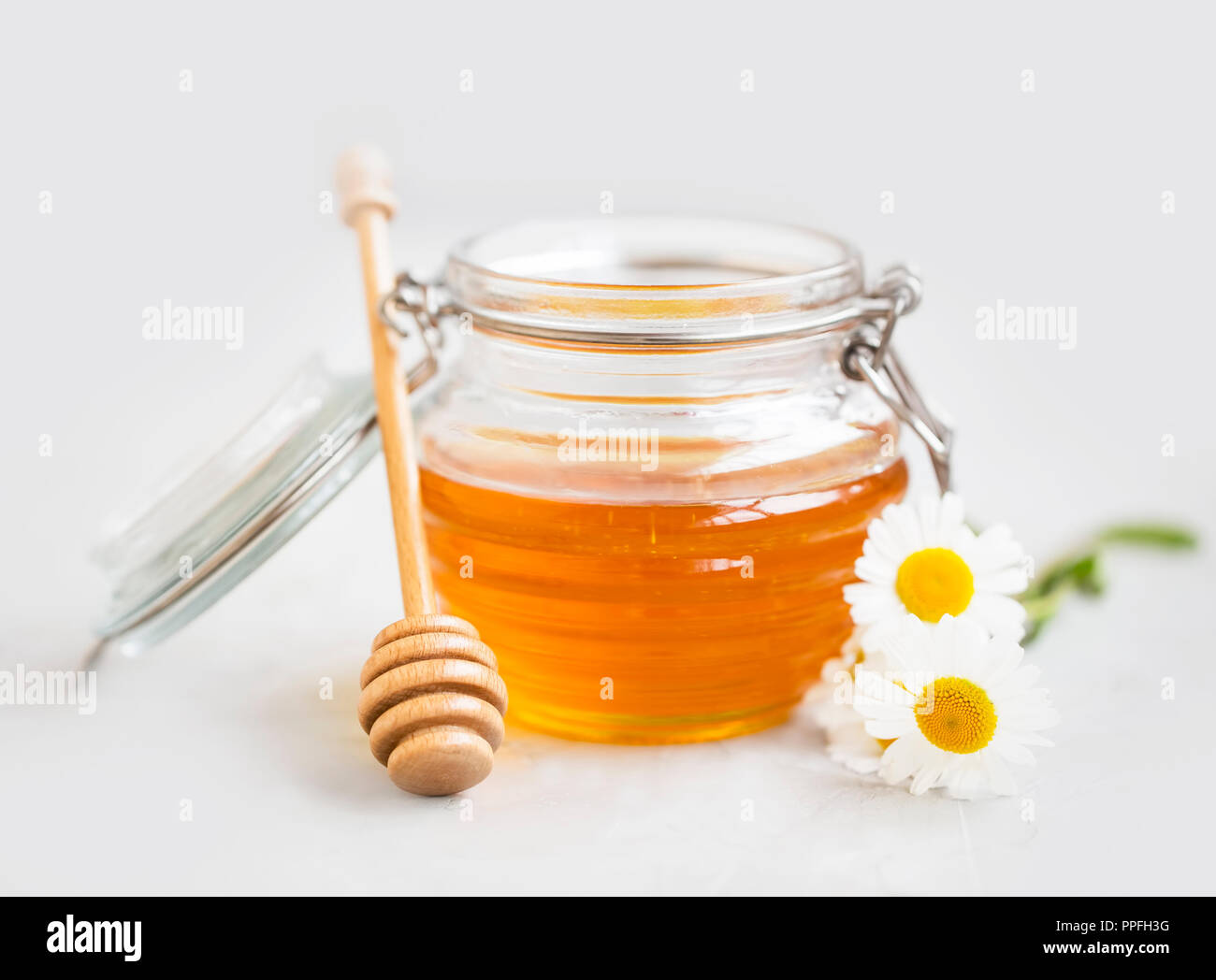 Materie miele biologico in un vasetto con bilanciere e fiori, sano dolcificante naturale Foto Stock