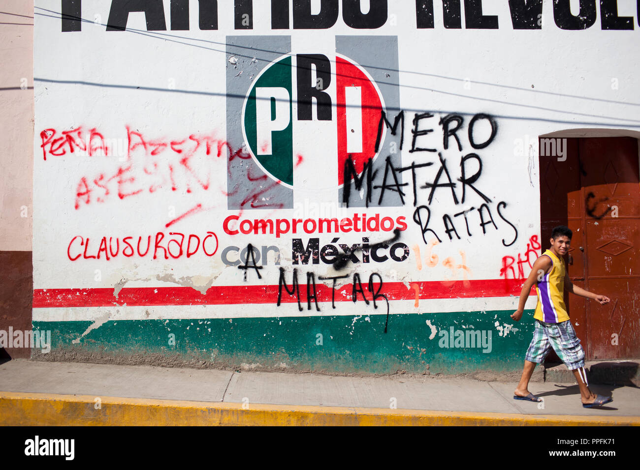 Un uomo cammina passato gli uffici del PRI ufficio politico (partito rivoluzionario istituzionale) in Tlapa, Guerrero, Messico, prima a marzo a sostegno dei 43 studenti mancanti da Guerrero Stato che sono stati dispersi per quasi due mesi, il 15 novembre 2014. La legge grafitti " prima di uccidere i ratti'. Foto Stock
