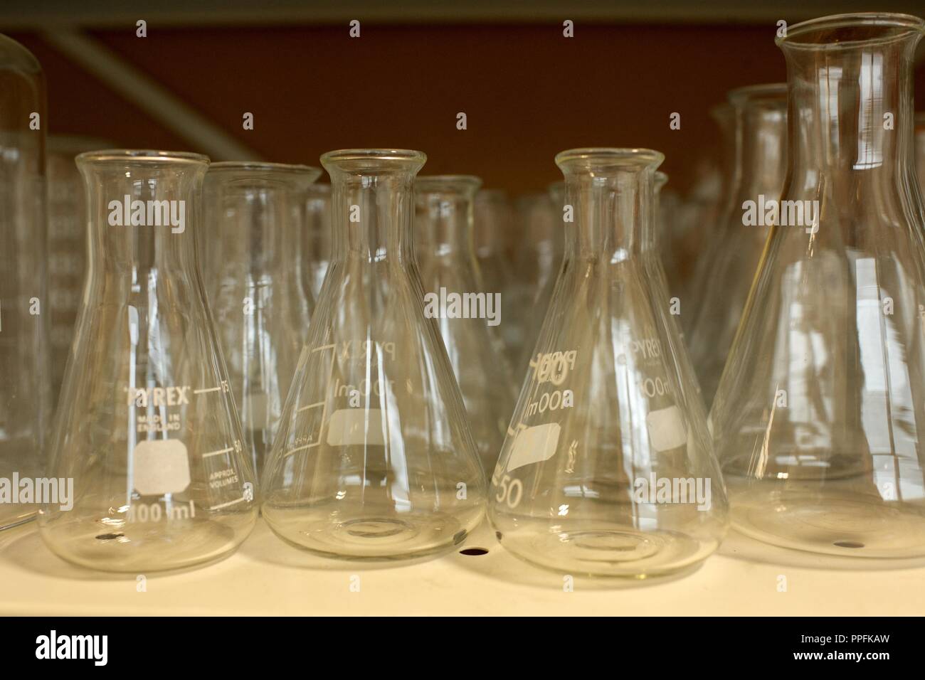 Matraccio di Erlenmeyer cilindri di vetro su un ripiano in un completo scuola laboratorio di chimica Foto Stock