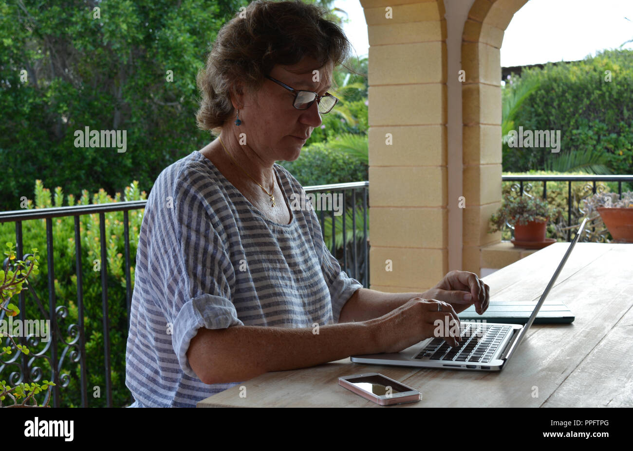 Donna che utilizza un computer portatile, seduti a un tavolo di legno su una terrazza. Foto Stock