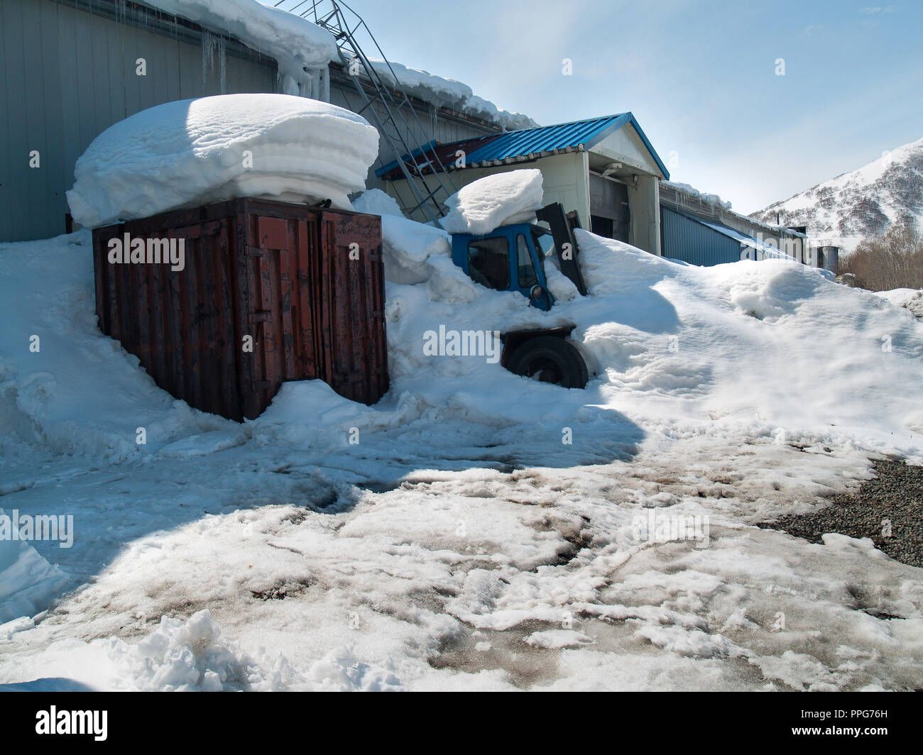 Coperte di neve impianti di produzione contro lo sfondo di una coperta di neve collina con ghiaccioli sul tetto in inverno in una giornata di sole Foto Stock