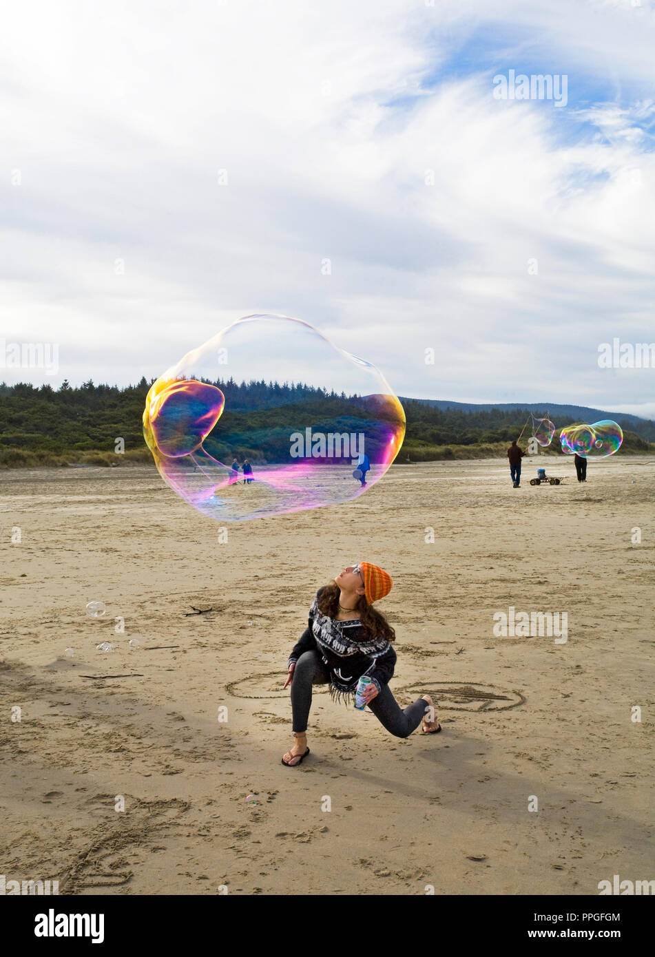 Una giovane donna cerca di mantenere una grande bolla di sapone in aria a un soffiaggio in bolla festa sulla spiaggia vicino Yachats, Oregon. Foto Stock